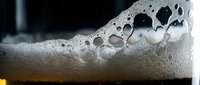Close-up macro shot of golden beer foam with bubbles creating texture and depth. Refreshing alcoholic beverage photography for commercial use.