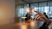 Hand holding transparent tablet displaying glowing gear icons in modern office conference room with blurred colleagues in background, representing digital technology and business innovation.
