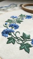 Hand embroidered blue flowers with green leaves on white linen fabric in wooden hoop, traditional needlework craft project for home decor and textile art.