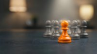 Orange pawn standing out among gray pawns on chessboard, symbolizing leadership, uniqueness, and competitive strategy for business concepts.