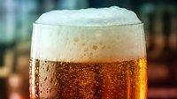 Chilled cola or dark beer in glass with thick foam head and condensation droplets, carbonated beverage for refreshment and social occasions.