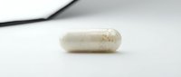 White capsule supplement pill with natural ingredients on neutral background for healthcare and wellness content.