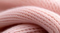 Soft pink knitted fabric macro shot showing detailed texture of wool or cotton yarn with gentle curves and intricate stitch pattern in pastel tones.