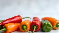 Fresh colorful bell peppers in red, orange and green arranged on white surface for cooking, healthy eating and organic vegetable concepts.