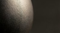 Curved metallic surface with fine textured finish creating dramatic light and shadow contrast for modern industrial design applications.