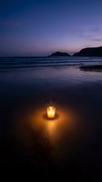 Glowing candle on sandy beach at twilight with purple sky and ocean waves creating peaceful romantic atmosphere for meditation and relaxation.
