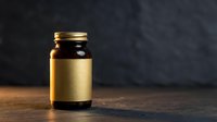 Amber glass medicine bottle with gold label on wooden surface against dark background for pharmaceutical and healthcare product packaging design.
