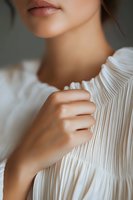 Close-up portrait showing delicate feminine details - partial view of lips, neck and hands against pleated white fabric in soft natural lighting. Perfect for beauty and fashion.