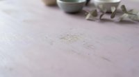 Overhead view of a pale lavender wooden surface with scattered eucalyptus leaves and small ceramic vessels, suitable for wellness, spa, and lifestyle product photography.