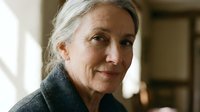 Senior Caucasian woman with gray hair smiling warmly in cozy indoor setting. Mature female portrait showing confidence and wisdom for lifestyle content.