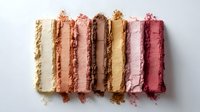 Crushed makeup powder samples in nude and pink tones arranged in straight lines showing texture and pigment intensity on white background for cosmetic industry use.