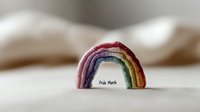 Pride month rainbow decoration on soft neutral background. Handmade textile arch in LGBTQ+ flag colors creates minimalist composition with gentle bokeh effect.