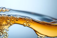 Dynamic wave of golden liquid with rising bubbles against blue background, macro photography showing fluid motion and surface tension in abstract composition.