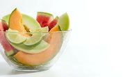 Fresh melon slices and lime arranged in glass bowl on white background, ideal for healthy eating, nutrition, and food styling projects.