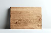 Wooden oak cutting board with natural grain texture and knots leaning against white wall on light surface. Clean minimalist kitchen background.