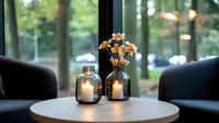 Cozy restaurant interior with glowing candle holders and dried flowers on round white table between armchairs, window view to green park. Atmospheric evening setup.