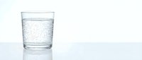Clear glass filled with sparkling carbonated water showing effervescent bubbles on clean white surface for beverage and refreshment concepts.