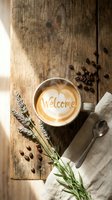 Steaming cappuccino with welcome latte art heart on rustic wooden table, lavender sprigs, coffee beans, and linen napkin in warm morning light.
