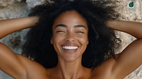 Young African American woman with natural curly hair laughing joyfully with closed eyes, expressing genuine happiness and positive emotions against blurred background.