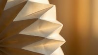Modern origami paper lamp shade with geometric pleated design creating warm ambient lighting for contemporary interior decor and home decoration.