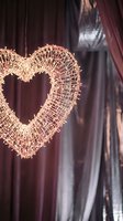 Wicker heart-shaped decoration with warm LED lights hanging indoors creates romantic atmosphere for Valentine's Day celebration and wedding decor.