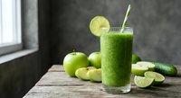 Fresh green smoothie with lime slice and straw surrounded by green apples and lime wedges on wooden table for healthy lifestyle and nutrition.