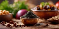 Black powder spice in copper bowl on rustic wooden surface with scattered ingredients, herbs and spices in background, moody food photography composition.