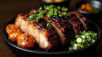Succulent grilled pork belly slices with crispy skin, glazed in sweet soy sauce, garnished with fresh chopped green onions, served on black plate with side dishes.