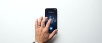 Senior man's hand holding smartphone displaying stock market graph with upward trend line on screen against white background.