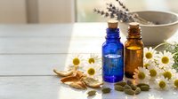 Essential oils in blue and amber bottles with chamomile flowers, lavender and herbs on white wooden table for aromatherapy and natural wellness treatments.