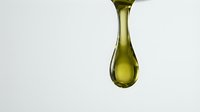Golden olive oil drop falling against clean white background showcasing natural liquid texture and purity for culinary and wellness applications.
