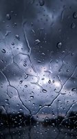 Water droplets on glass surface creating abstract patterns during rainy weather with blurred background and atmospheric lighting effects.