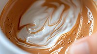 Swirling caramel and cream create mesmerizing patterns in macro photography, showing rich texture and smooth blending of warm brown and white colors in liquid form.