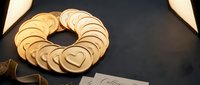 Stacked golden heart-shaped cookies arranged in a circle with ribbon on dark surface, suitable for Valentine's Day, wedding, and celebration designs.