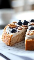 Slice of vanilla cake topped with cream frosting, fresh blueberries and walnuts on white surface. Close up macro shot with selective focus and blurred background.