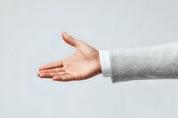 Professional male hand in business suit sleeve extending for handshake against light background, showing trust and partnership in corporate environment.