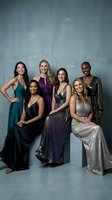 Diverse group of six women in elegant evening gowns posing together for formal portrait against textured gray backdrop for special occasion celebration.