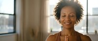 Woman with curly hair smiling indoors near windows, wearing brown shirt. Professional portrait for business, corporate, lifestyle, and wellness content.