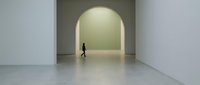 Woman in dark clothing walking through minimalist corridor with arched doorway and glowing green wall, modern interior design and contemporary architecture concept.