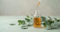 Eucalyptus essential oil in glass bottle with dropper and fresh green leaves on neutral background for aromatherapy and natural wellness treatments.