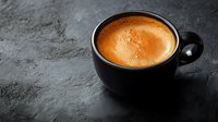 Fresh espresso with golden crema in black ceramic cup on dark textured background. Minimalist coffee composition with dramatic lighting and copy space.