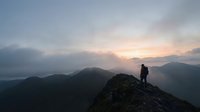 Silhouette of hiker standing on mountain peak at sunrise with misty valleys and distant mountains in background, adventure and exploration concept.