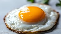 Macro shot of sunny side up fried egg with crispy edges and bright orange yolk on light background, fresh breakfast food photography.