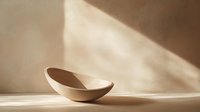 Minimalist ceramic bowl in warm beige tones with dramatic diagonal shadows on neutral background, artistic still life composition highlighting shape and light.