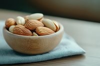 Wooden bowl filled with fresh almonds on blue linen cloth, healthy snacking and natural nutrition concept for cooking and wellness lifestyle.