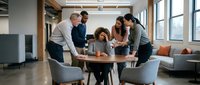Diverse business team collaborating around conference table in modern office space with natural lighting and contemporary furniture for meetings.