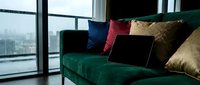 Modern emerald green velvet sofa with colorful throw pillows in contemporary apartment living room with large windows overlooking city skyline.