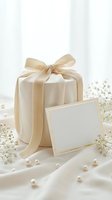 Elegant cream gift box with satin ribbon bow and blank card surrounded by pearls and delicate flowers for special occasions and celebrations.