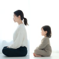 Asian mother and young daughter practicing meditation together in bright minimalist room, sitting cross-legged in peaceful mindfulness pose for wellness.