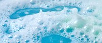 Foamy white soap bubbles and suds floating on bright blue water surface creating refreshing cleansing and hygiene concept for bathroom and spa applications.